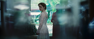 A woman in a wedding dress looks over her shoulder. Her surroundings are green and blurry.