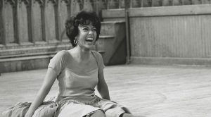 Archival photo of woman laughing on floor wearing dress and big hoops.