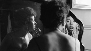 Archival photo of woman applying lipstick in the mirror. We see the woman's back and two different reflections.