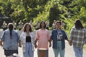 A group of Mohawk women hold hands forming a chain and looking directly into the camera.