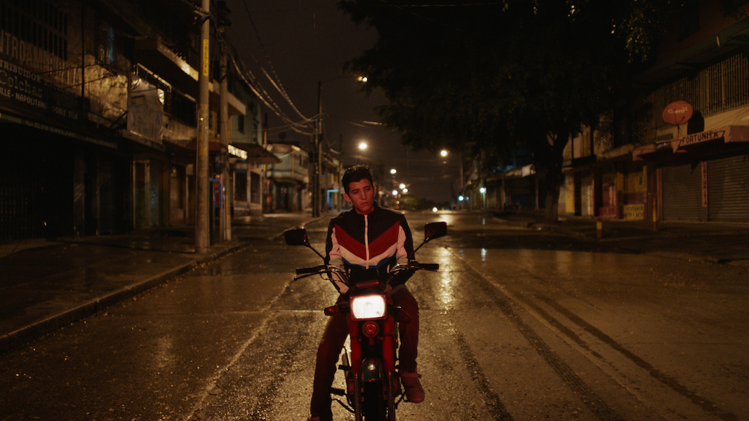 Young man is sitting on motorcycle with his arms on his lap. The street is empty.