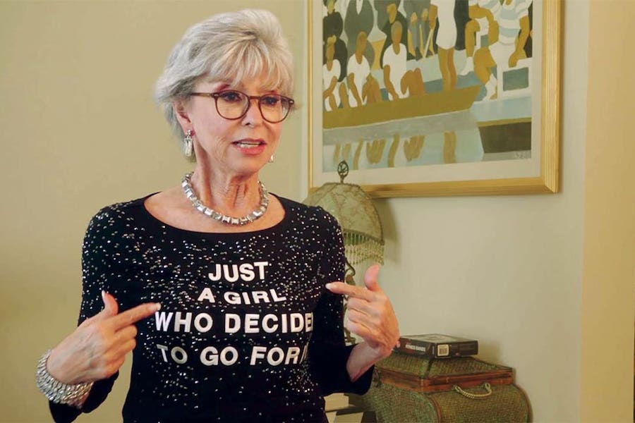 A woman points at her shirt which says, "just a girl who decided to go for it"