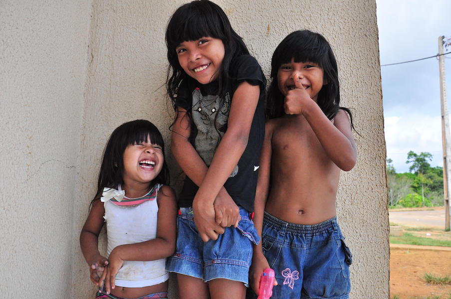Three children with long black hair and bangs are shy but giggling.