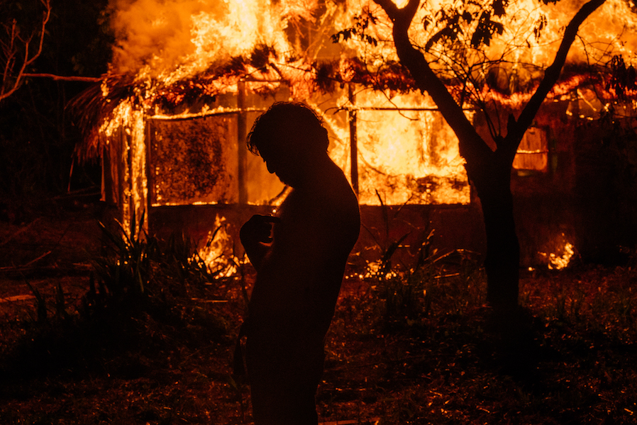 A persons dark silhouette is visible in front of a blazing fire. 