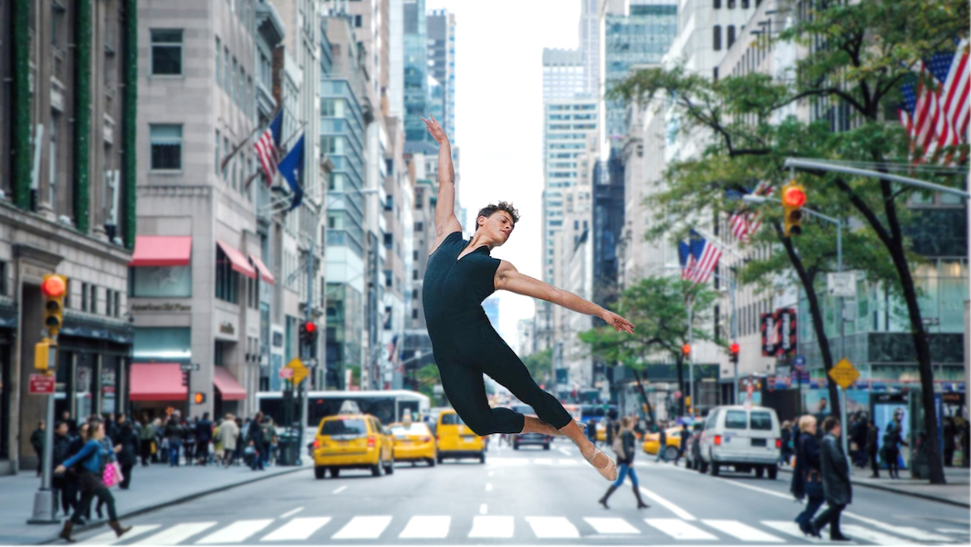 [Image Description: An image from the documentary, CUBAN DANCER, shows a young person wearing a blue unitard and beige ballet shoes jumping elegantly in the middle of a NYC crosswalk. Pedestrians and cabs are out of focus in the background.]