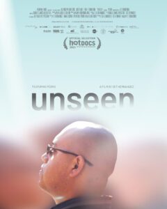 Poster with a side profile shot of Pedro, a bald young man with glasses wearing a black collared shirt on a sunny day. The background is out of focus and gas the text "unseen."